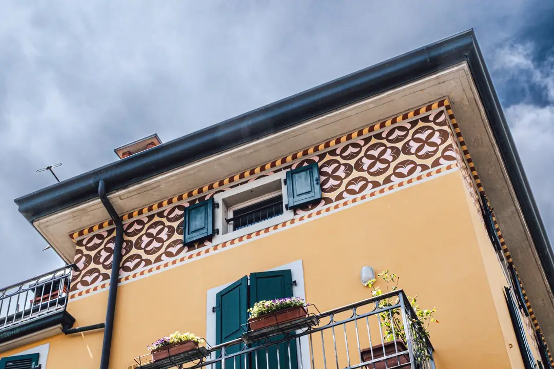 Facciata gialla con persiane verdi e fregio decorativo